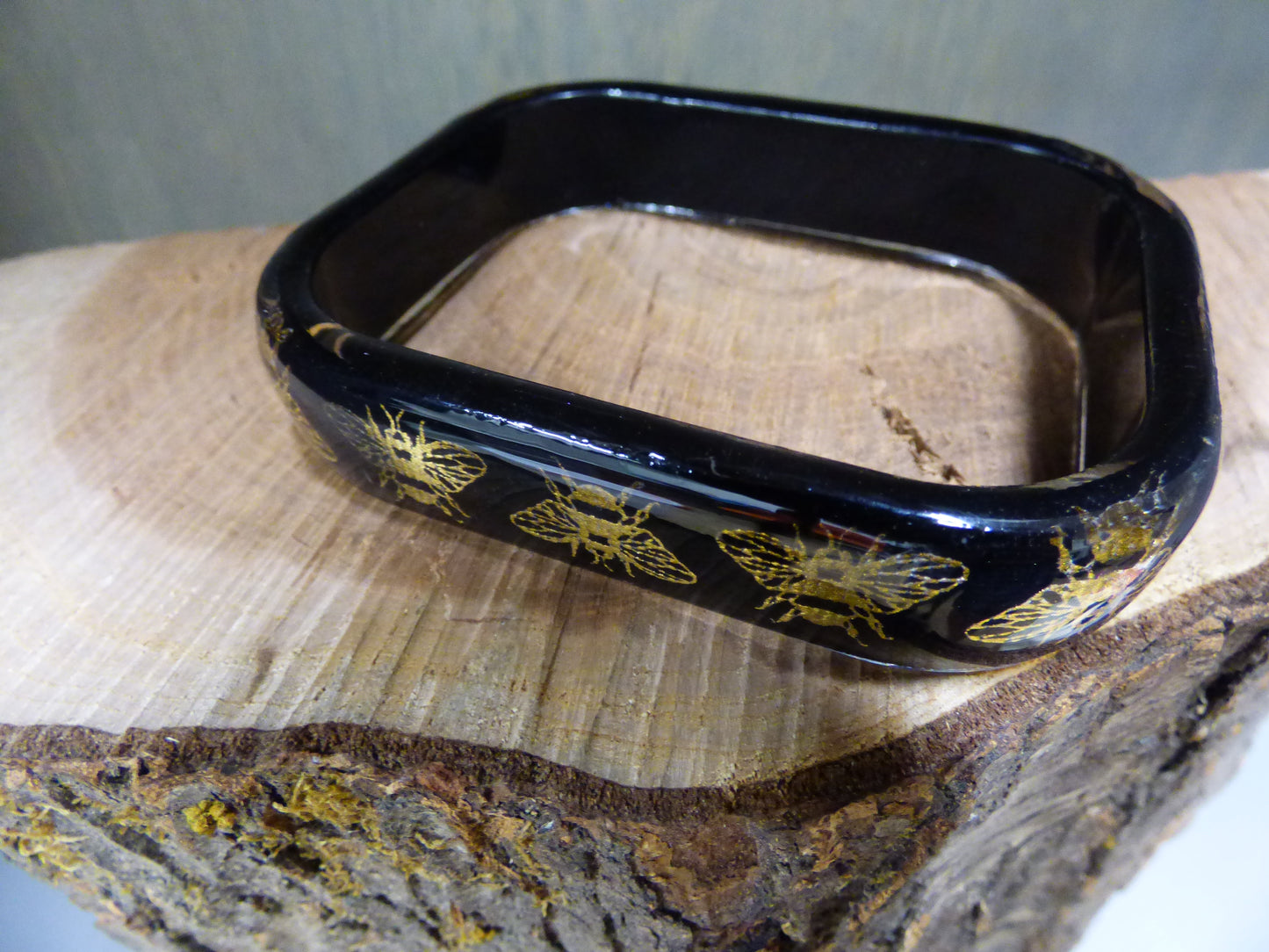 Black rectangular object with gold bee designs on a wooden surface