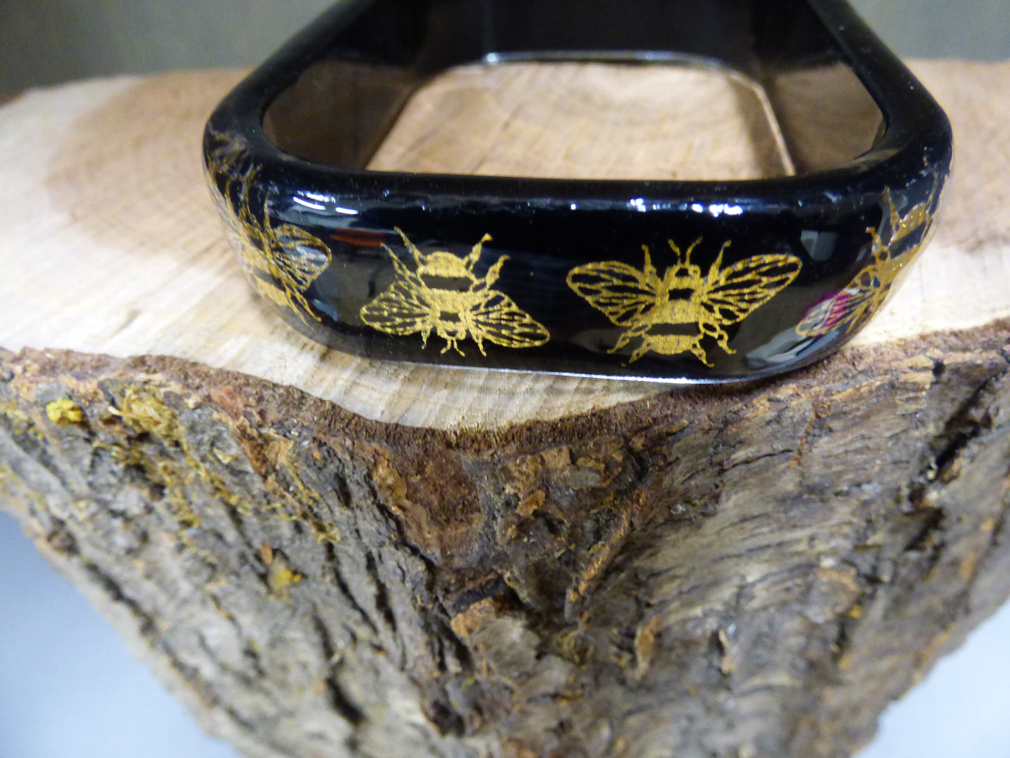 Black rectangular object with gold bee designs on a wooden surface