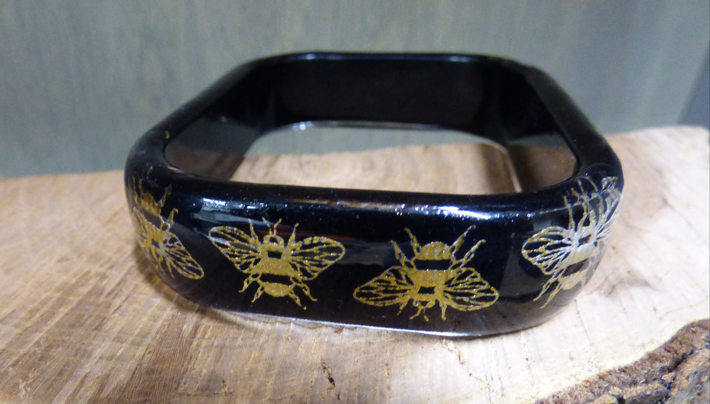 Black rectangular object with gold bee designs on a wooden surface