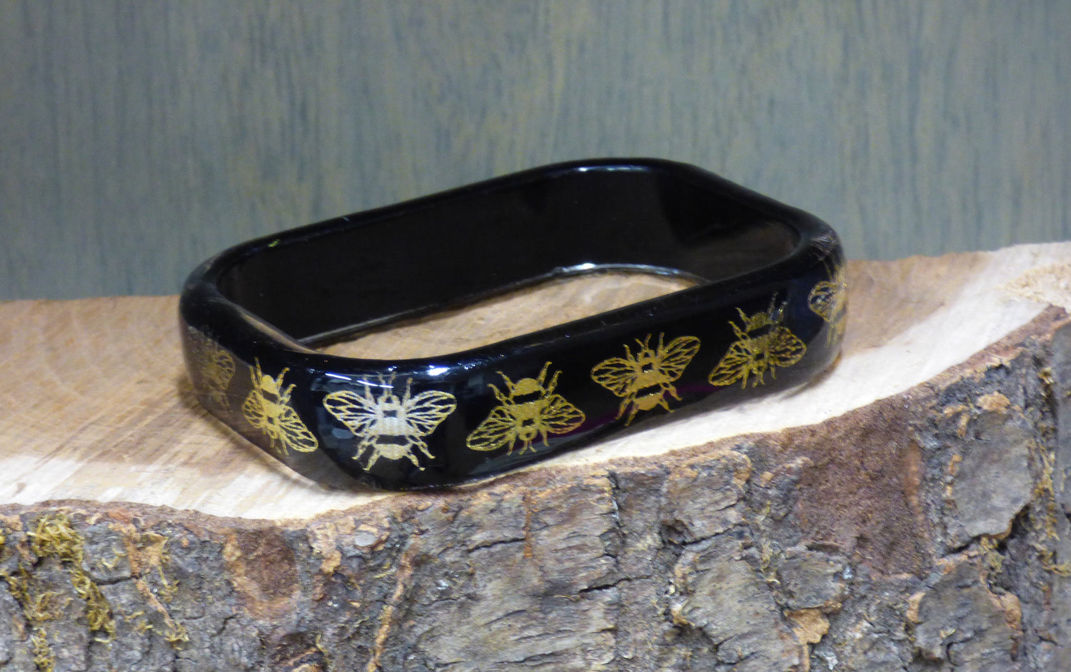Black rectangular object with gold bee designs on a wooden surface