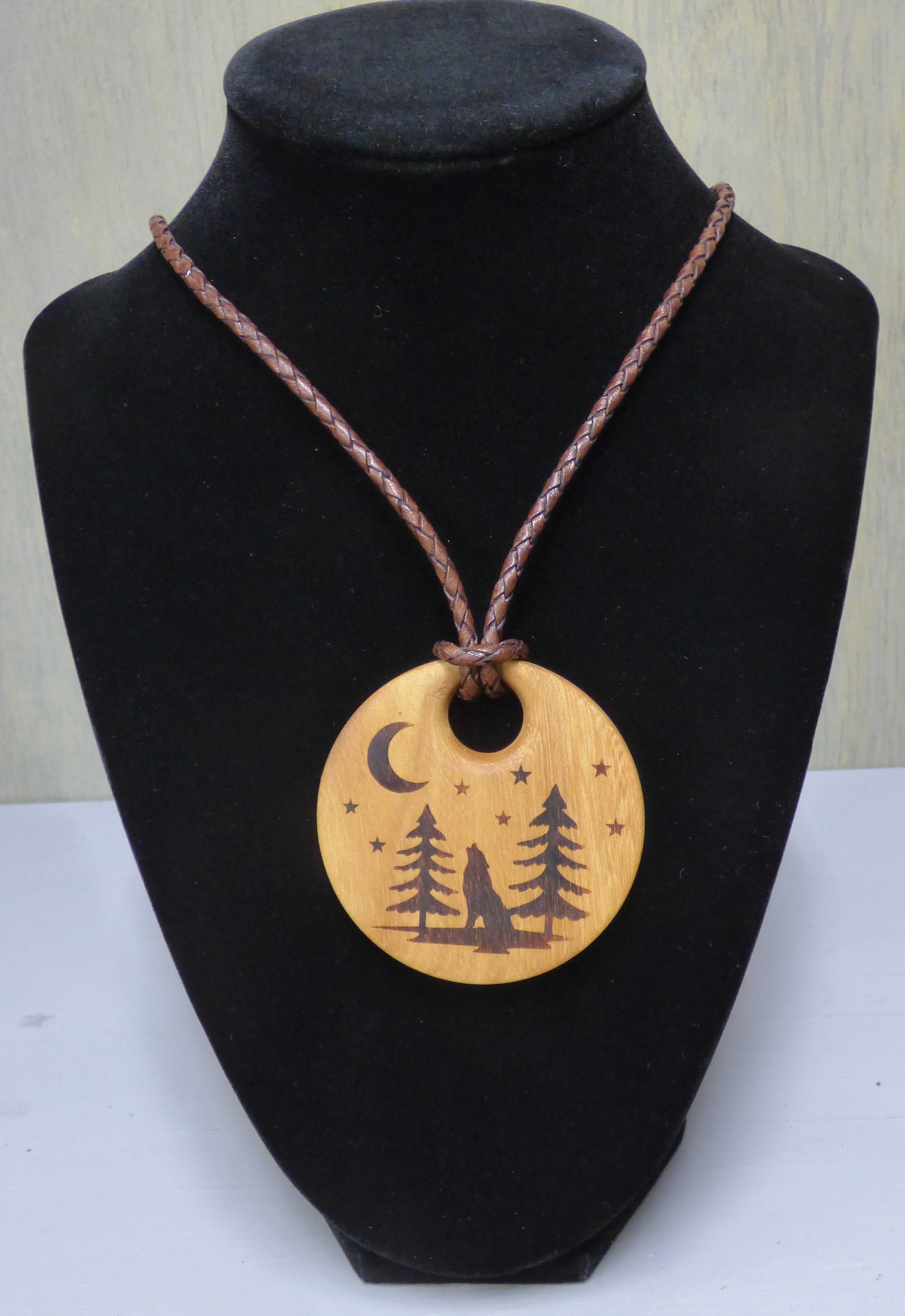 Necklace with a wooden pendant featuring nature-themed design on a black bust.