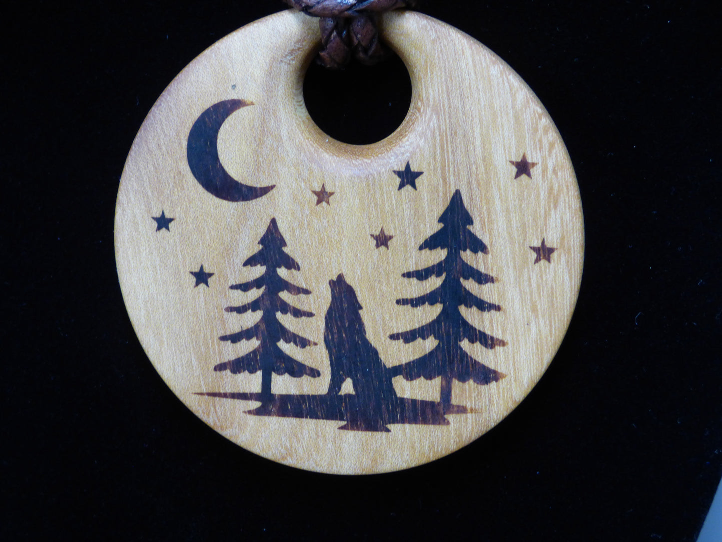 Wooden pendant with wolf and trees design on a black background