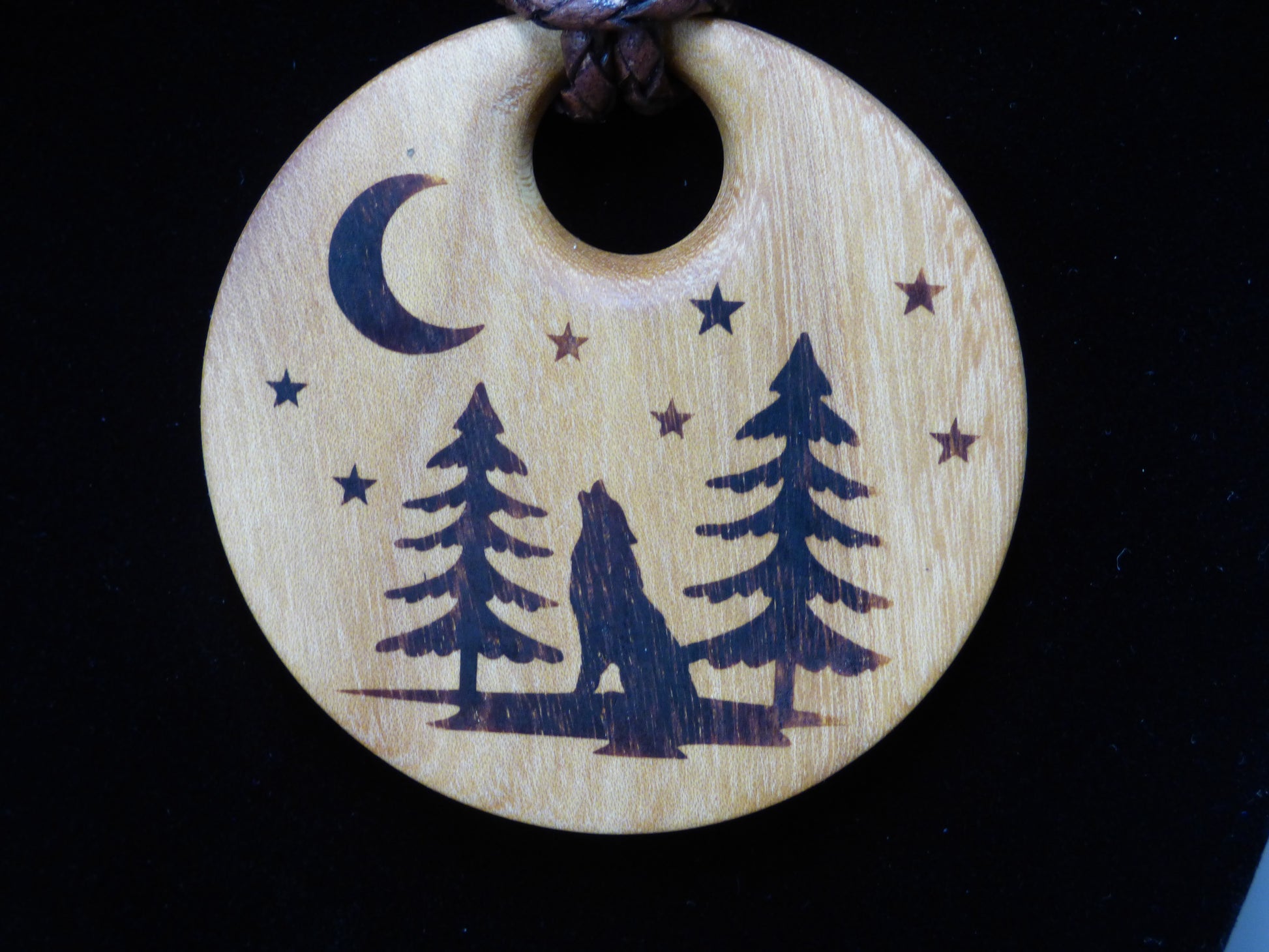 Wooden pendant with wolf and trees design on a black background