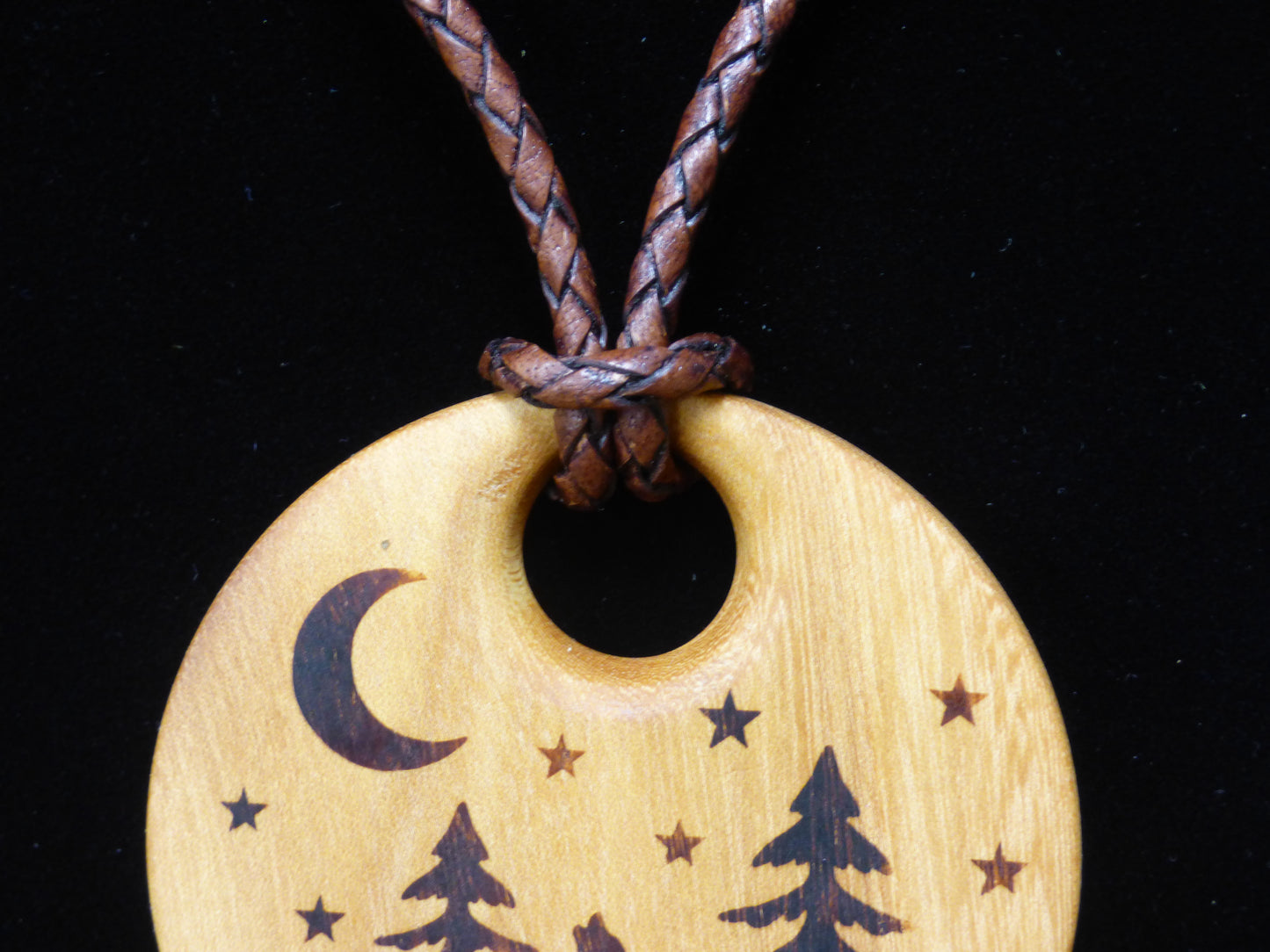 Wooden pendant with moon and wolf design on a braided leather cord against a black background
