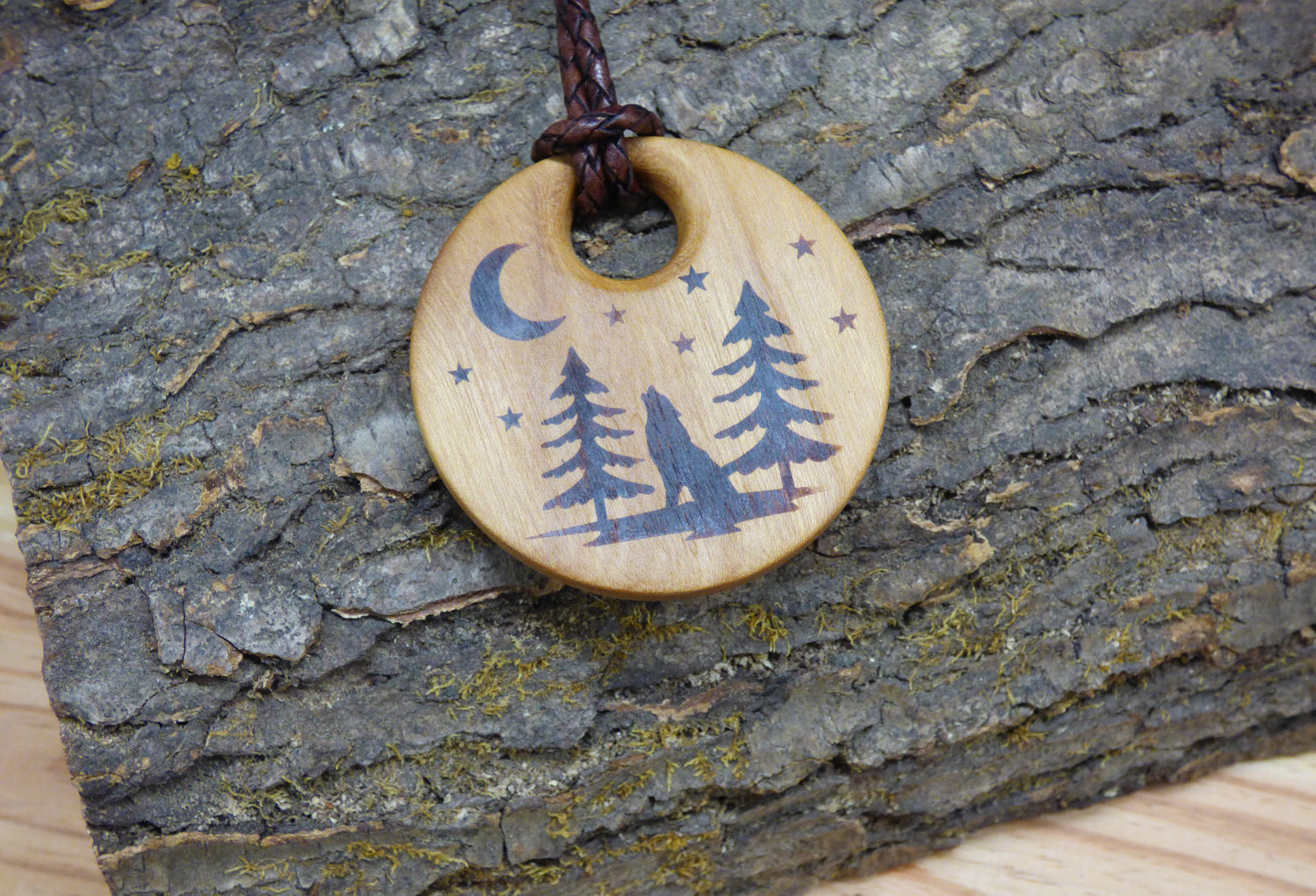 Wooden pendant with wolf and tree design against a wood log