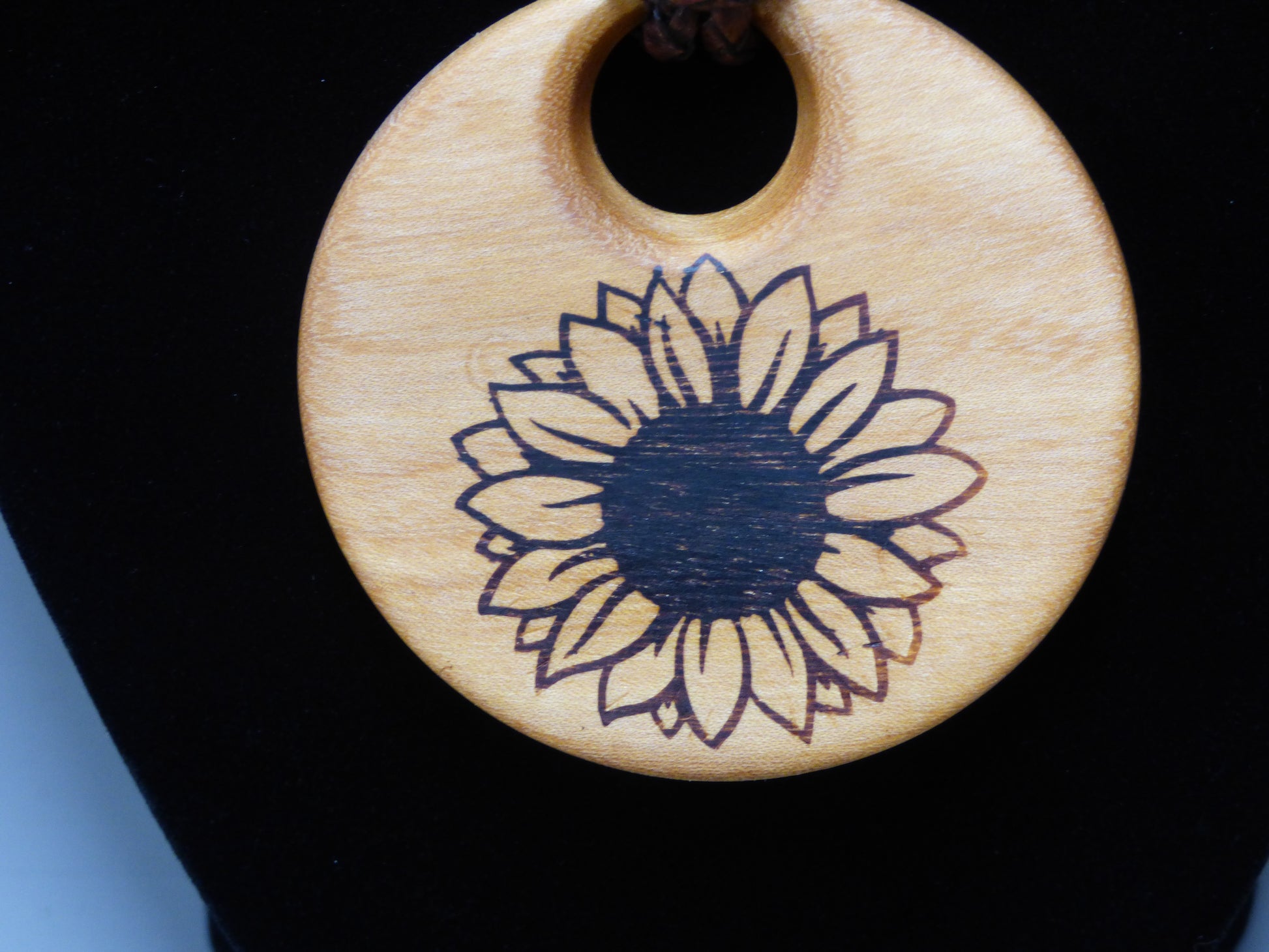 Wooden pendant with a sunflower design on a black background